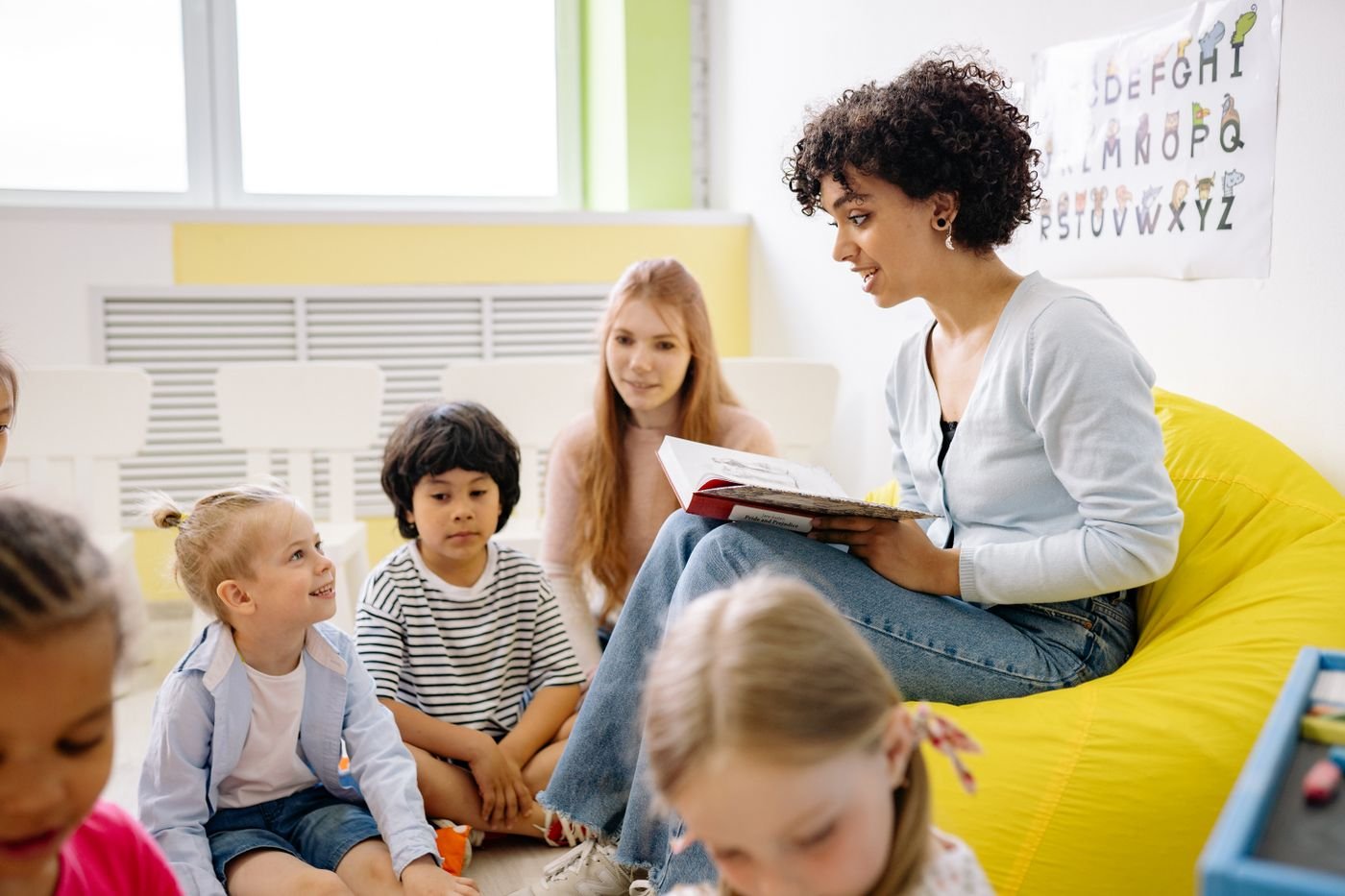 Caregiver reading a picture book to a toddler in a cosy crèche corner